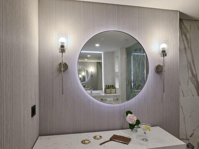 Moderner Badezimmerspiegel mit LED-Beleuchtung, zwei Wandleuchten und Marmor-Waschtisch mit Dekoration.