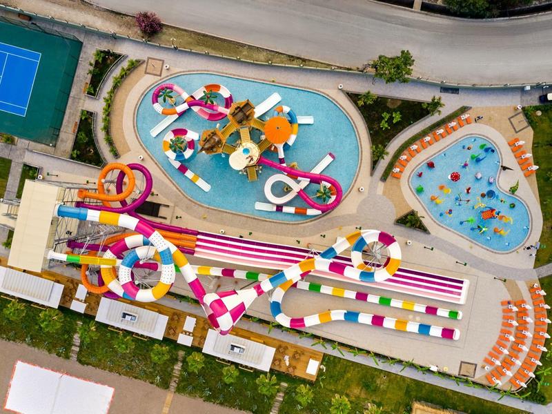 Bunter Freizeitpark mit Wasserrutschen, Pools und Liegestühlen aus der Vogelperspektive.
