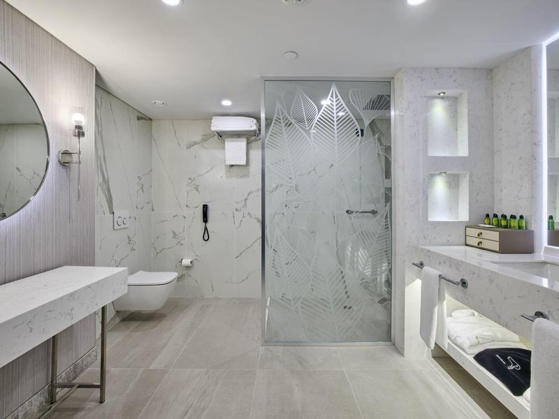 Helles Badezimmer mit Walk-In-Dusche, rundem Spiegel, Wand-WC und modernen weißen Fliesen.