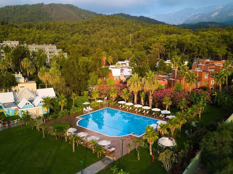 Großer blauer Pool mit Liegen, umgeben von grünen Bäumen und Hügeln im Hintergrund.