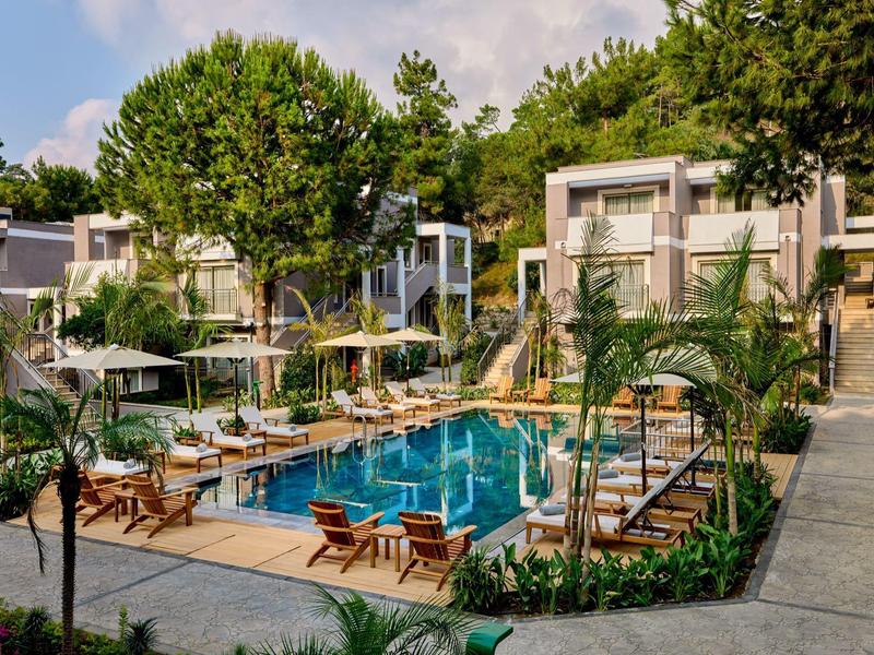 Moderner Poolbereich mit Liegestühlen, Sonnenschirmen und Bäumen in einer ruhigen Ferienanlage.