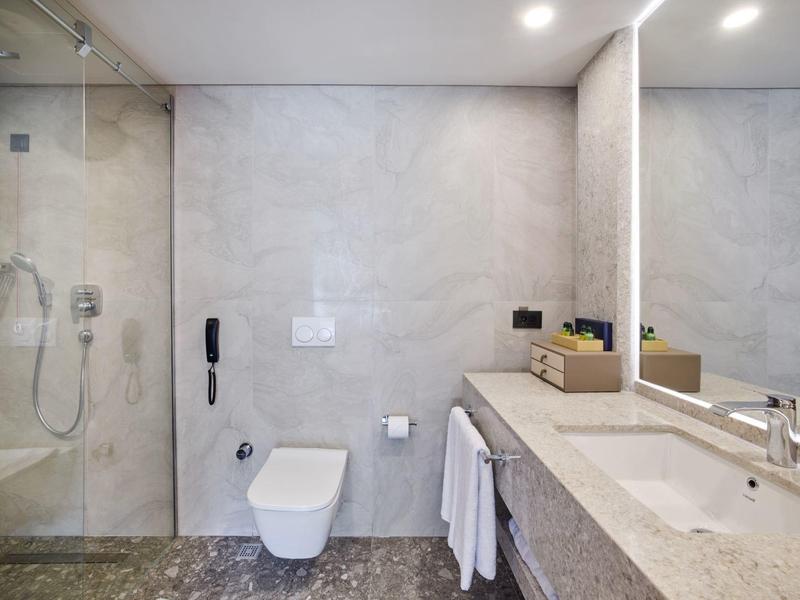 Moderne, helle Badezimmer mit grauen Fliesen, Dusche, Toilette, großem Spiegel und Waschtisch.