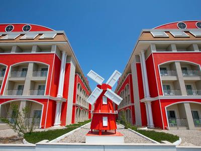 Due edifici rossi con balconi bianchi e un piccolo mulino a vento tra di loro sotto un cielo blu.