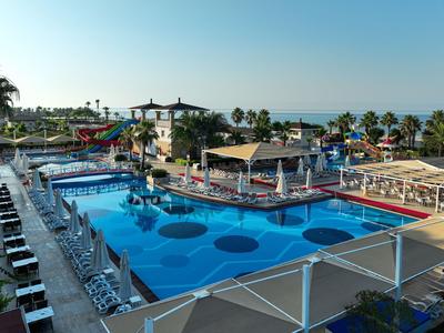 Großer Außenpool mit blauer Wasserfläche und Sonnenliegen in Hotelanlage am Meer.