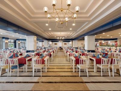 Großer, heller Speisesaal mit weißen Stühlen und roten Tischdecken in einem Hotel.