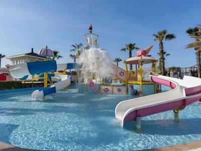 Wasserrutschen und Palmen umgeben einen Kinderpool bei klarem Himmel in einem Ferienresort.