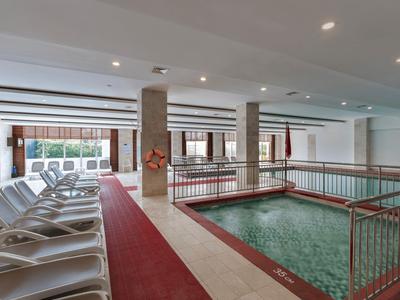 Innenpoolbereich mit Liegestühlen, roten Teppich und weißen Wänden in einem Hotel.