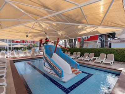 Kinderpool mit kleinem Bootsrutsche und Liegestühlen unter einem großen Sonnensegel.