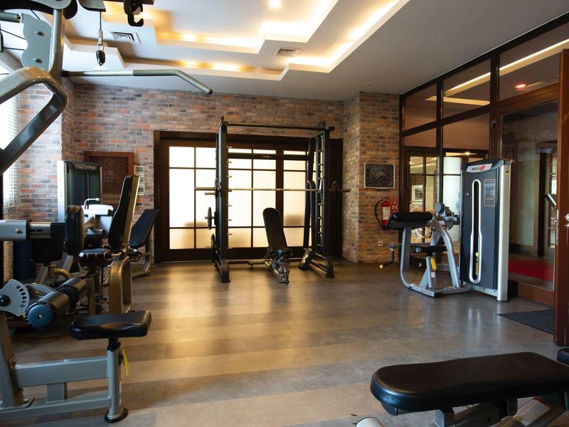 Gimnasio moderno con máquinas de ejercicio y suelo de madera junto a una pared de ladrillos.