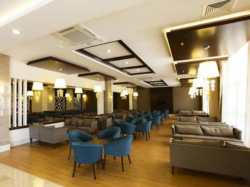 Przestronny salon hotelowy z niebieskimi fotelami i brązowymi kanapami na jasnej podłodze.