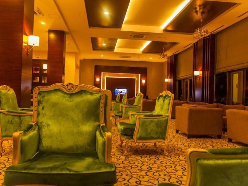 Jasny salon hotelowy z zielonymi fotelami i wzorzystym dywanem.