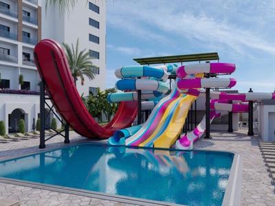 Bunte Wasserrutschen führen in einen außenliegenden Pool neben einem Hotelgebäude.