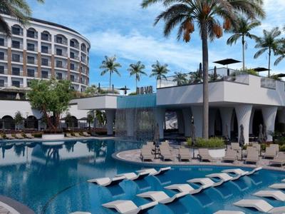 Moderner Hotelpool mit Liegestühlen, Palmen und mehrstöckigem Gebäude im Hintergrund.