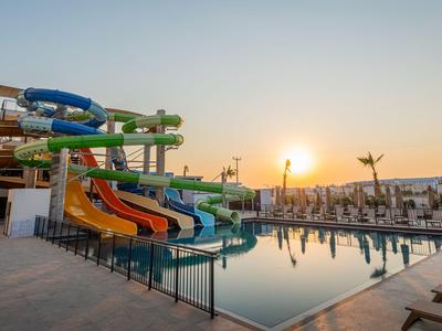 Mehrfarbige Wasserrutschen neben einem Pool bei Sonnenuntergang in einem Hotelresort.