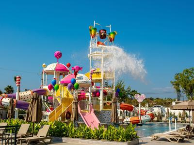 Bunter Wasserpark mit Rutschen, Spritzfiguren und Liegestühlen unter klarem, blauem Himmel.