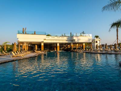 Moderner Poolbereich eines Hotels mit Liegestühlen und Palmen bei Sonnenuntergang.