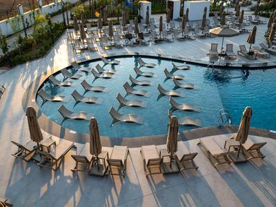 Großer Hotelpool mit Sonnenliegen und Sonnenschirmen auf einer Terrasse am Wasser.