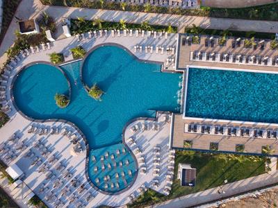 Vogelperspektive eines Hotels mit zwei großen Pools und vielen Liegestühlen.