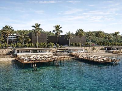 Acqua chiara e piattaforme in legno davanti a un hotel con palme e cielo nuvoloso.