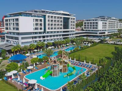 Complexe hôtelier moderne avec piscine extérieure, aire de jeux pour enfants et transats sous un ciel bleu.