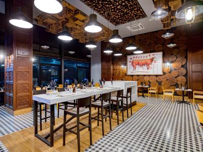 Salle à manger moderne avec panneaux en bois, grandes tables et éclairage chaleureux dans un restaurant.