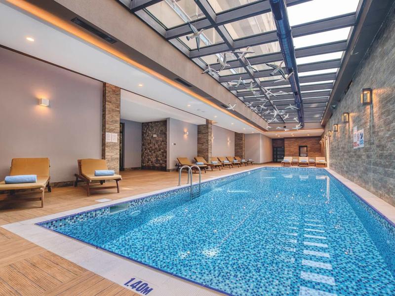 Piscine intérieure chauffée avec chaises longues et éclairage moderne sous une toiture en verre.