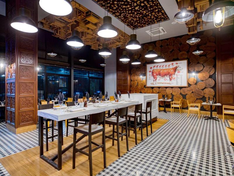Salle à manger moderne avec panneaux en bois, grandes tables et éclairage chaleureux dans un restaurant.