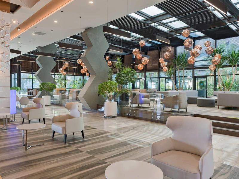 Hall d'hôtel moderne avec sièges confortables, grandes plantes et éléments d'éclairage décoratifs.