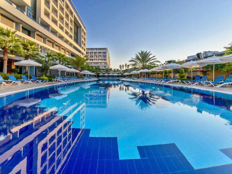 Grande piscine d'hôtel avec chaises longues bleues et parasols sous un ciel dégagé.