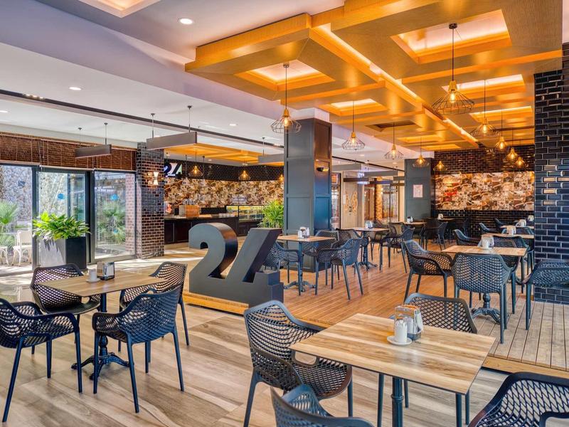 Restaurant moderne avec tables en bois, chaises noires et éclairage jaune distinctif au plafond.