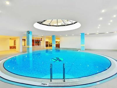 Rundes Hallenbad mit blauem Wasser, großer Lichtkuppel und türkisfarbenen Säulen.