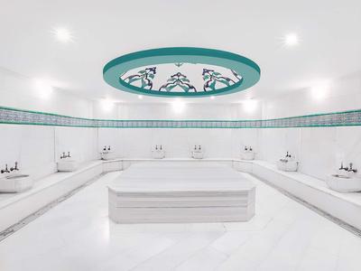 Großer weißer Hammam mit Marmor-Ottoman in der Mitte und türkisfarbener Deckenverzierung.