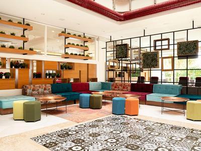 Großer, heller Raum mit bunten Sitzwürfeln, Sofas, Teppichen und vielen Pflanzen an den Wänden.