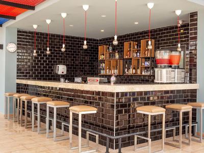 Moderner Tresen mit schwarzen Kacheln, Holzstühle und Regale mit Gläsern und Spendern.