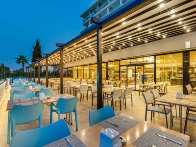 Große, moderne Terrasse mit blauen und grauen Stühlen, beleuchtet bei Dämmerung neben einem Glasgebäude.