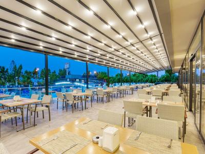 Offener Außenbereich eines Restaurants mit weißen Tischen, Stühlen und moderner Beleuchtung am Abend.