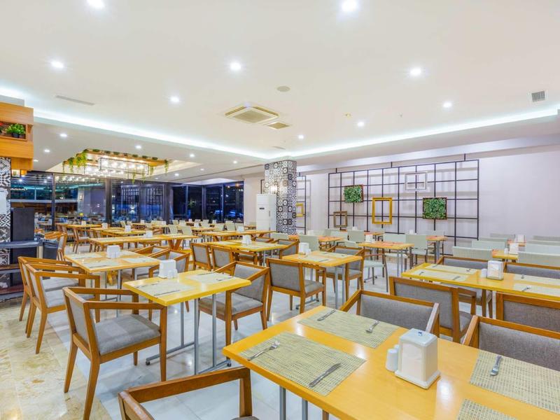 Modernes, helles Restaurant mit Holzstühlen, Tischen und eleganter Beleuchtung.