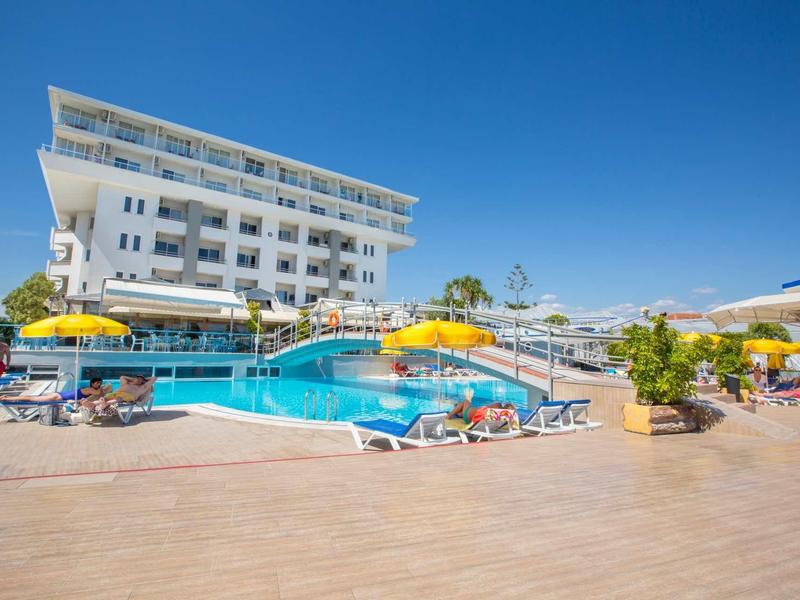 Moderner Hotelkomplex mit Pool, Sonnenschirmen und Liegestühlen unter klarem blauem Himmel.