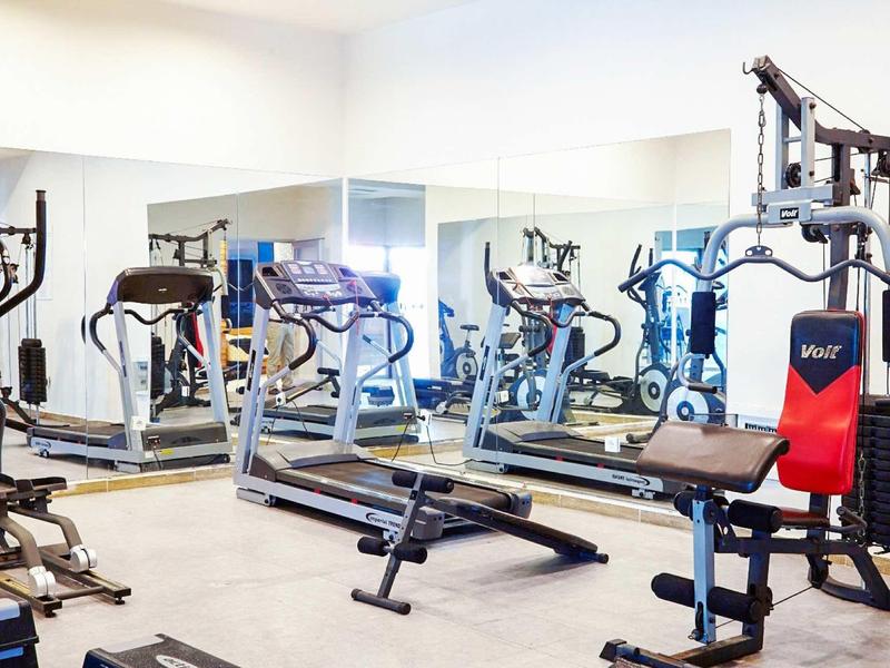 Helles Fitnessstudio mit Multigym, Laufband und Spiegelwand, ruhiger heller Raum.