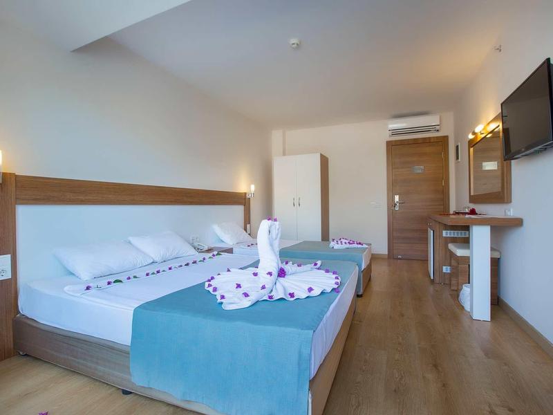 Helles Hotelzimmer mit Doppelbett, Holzboden, Wand-TV und Tisch mit Stühlen.