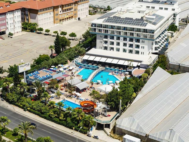 Großes Hotel mit blauem Pool, Wasserpark, umliegenden Gebäuden und grünen Bäumen.