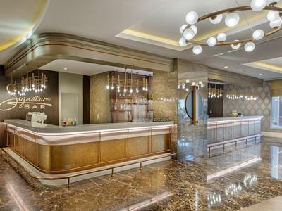 Recepción de hotel moderna con mostrador iluminado, suelo de mármol y iluminación elegante.