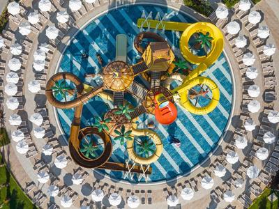 Vista aérea de un parque acuático con toboganes y piscina circular, rodeado de sombrillas y tumbonas.
