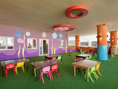 Zona infantil colorida con mesas pequeñas, sillas y decoraciones de pared en un hotel.