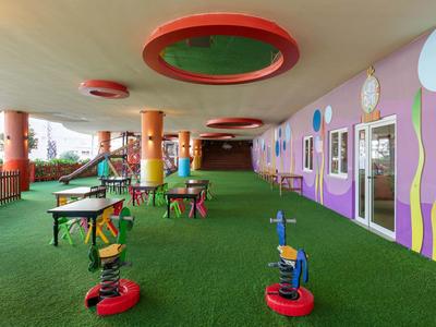 Área de juegos cubierta con estructura colorida y césped artificial verde en entorno hotelero.