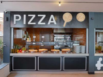 Pizzería moderna con cocina abierta y vista a la masa de pizza y horno de leña.