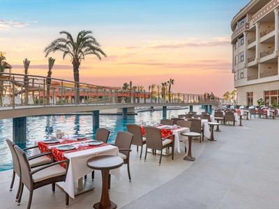 Terrasse avec tables dressées à côté d'une piscine devant un hôtel au coucher du soleil.