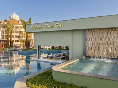 Área de piscina de lujo con bar junto a una cascada en un resort hotelero bajo cielo despejado.