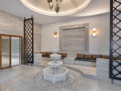 Lobby elegante de hotel con fuente de mármol, área de asientos y rejas metálicas decorativas.