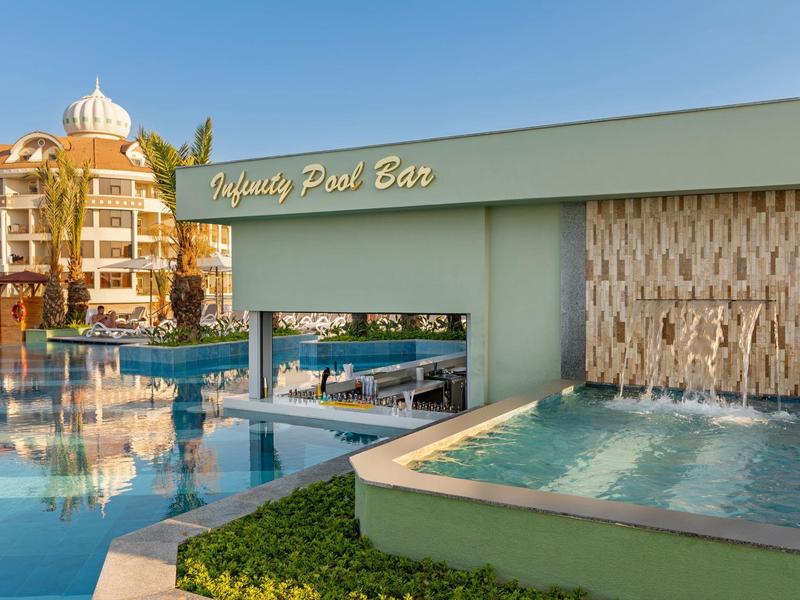 Piscina del hotel con pared de cascada y bar de piscina bajo cielo despejado al atardecer.